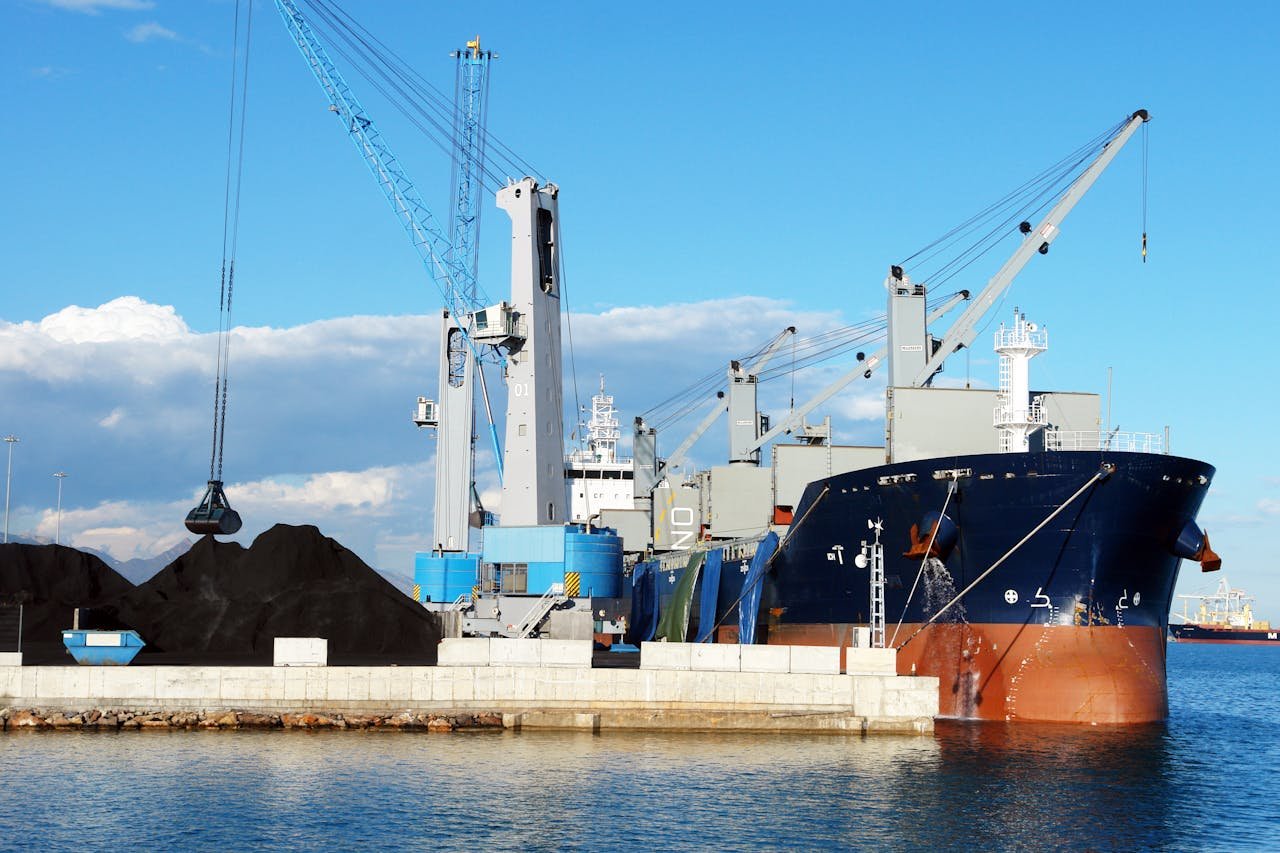 Cargo ship and cranes at an industrial port, loading minerals under a clear blue sky.